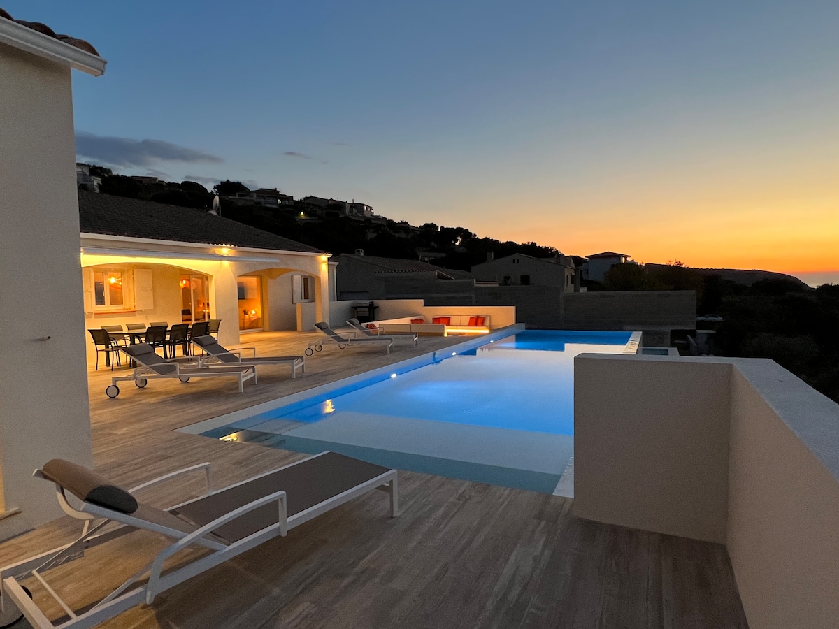 An outdoor terrace is displayed at dusk, featuring a heated swimming pool surrounded by lounge chairs. Soft lighting illuminates the area, creating a serene ambiance as the sun sets in the background, casting warm hues across the horizon.