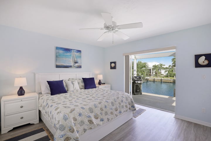 Spacious king bedroom featuring luxury linens, soft coastal décor, and direct access to the lanai and waterfront—perfect for waking up to peaceful water views every morning.