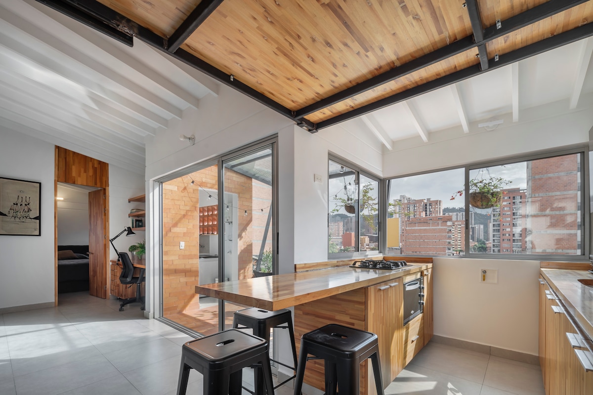 A spacious kitchen features wooden cabinetry and countertops with a gas stove included. Large glass sliding doors open to a balcony area. The room is illuminated by natural light, with a modern design that highlights the wood details in the ceiling and walls.