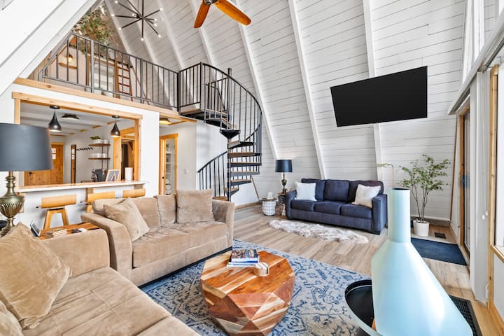 Main floor living room with couch seating for 9 people. 3 barstools along a countertop facing the kitchen where 3 more barstools sit. The blue couch is also a pull out bed with a double sized mattress.