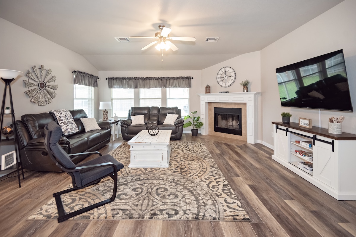 The living room is bright and spacious, featuring large windows that provide natural light. A cozy seating arrangement is set around a central coffee table, with a stylish area rug anchoring the space. A flat-screen TV is mounted on one wall, complemented by decorative accents.