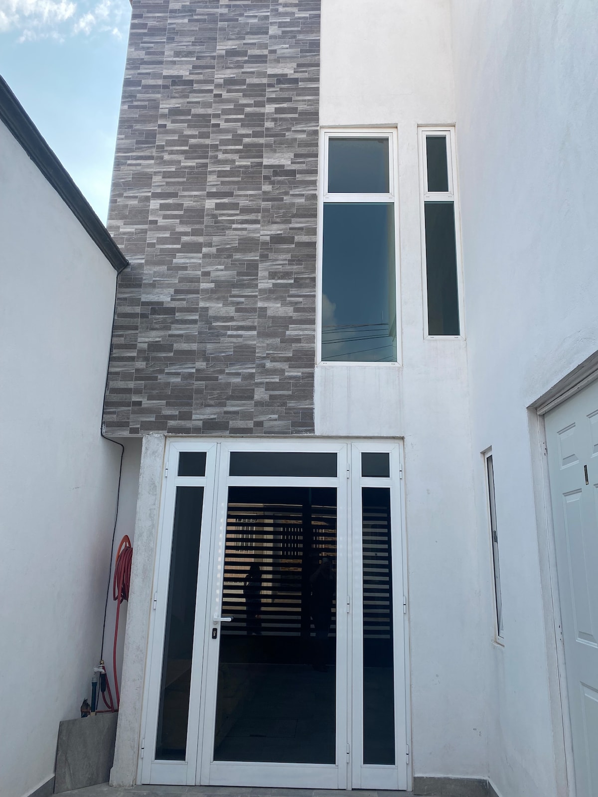 A modern entrance is highlighted by large glass doors framed in white and flanked by tall, narrow windows. The walls are a combination of smooth white texture and a patterned gray design, creating a visually interesting contrast.