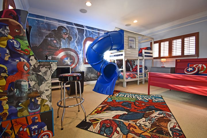 La sala temática Marvel tiene una cama de tamaño completo, litera con tobogán de tubo, Xbox One Series X configurada para 2 jugadores y una consola de videojuegos Maravillosos.