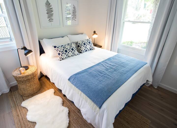 The blue bedroom features a queen bed, botanical art, and a faux sheepskin rug.