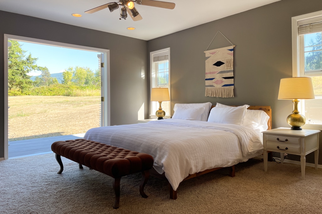 Главна спална соба со брачен кревет со поглед на задниот двор од 1 декар со зимзелен и поглед кон планината.