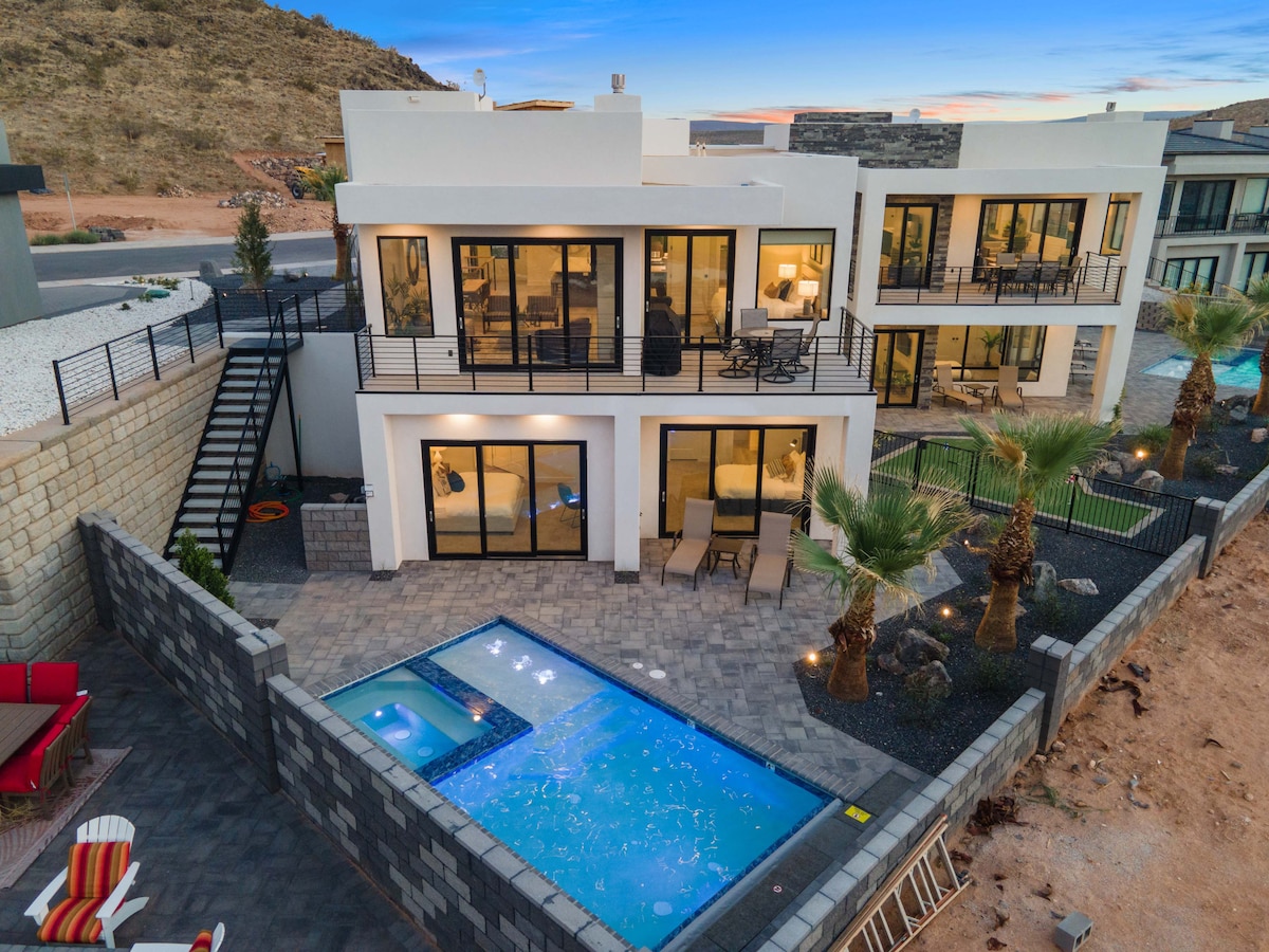 A modern townhome exterior showcases large glass doors and multiple outdoor seating areas. A private pool surrounded by lounge chairs is set within a manicured yard, highlighted by palm trees. An elegant balcony overlooks the pool area, providing additional outdoor space.