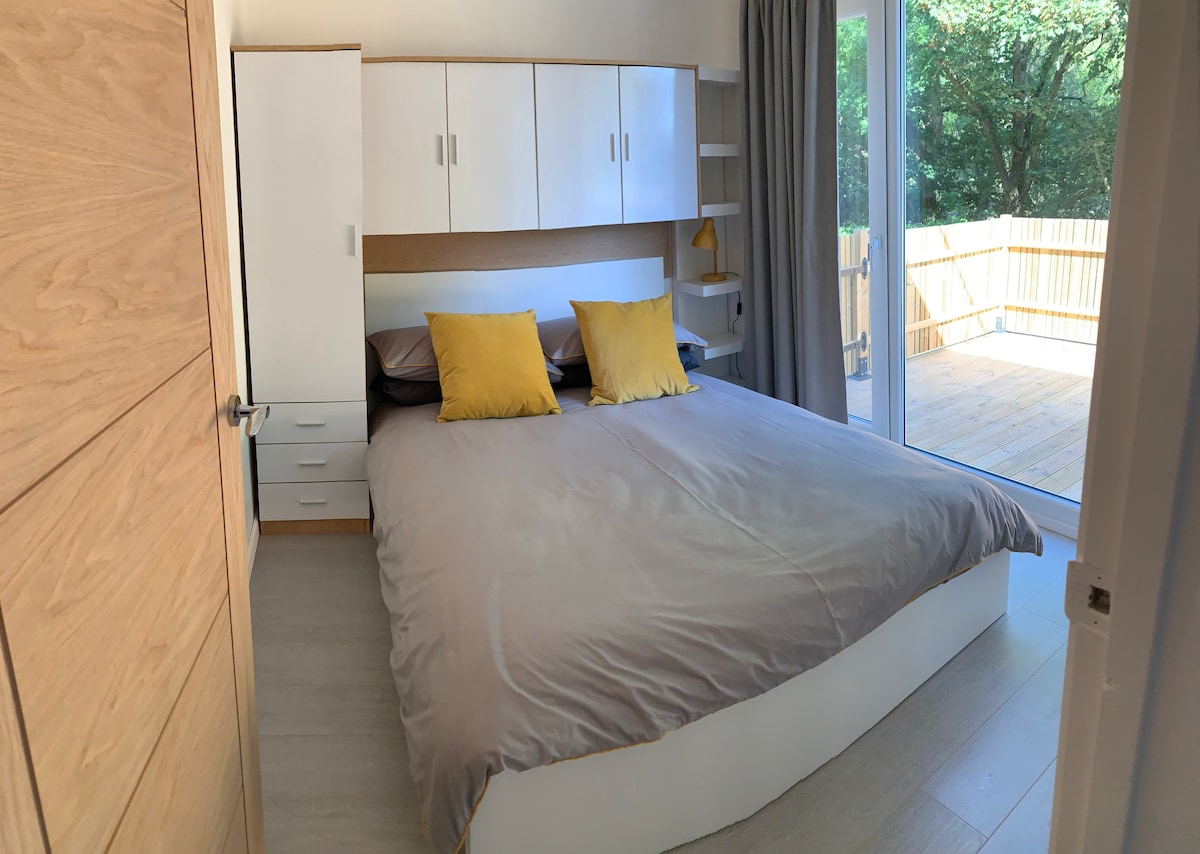 The comfortable main bedroom looks out onto a private raised decked area through full-height glazed windows. The bedroom is equipped with a double bed, plenty of built in storage and a USB charging plug. All bedding is included in your stay.