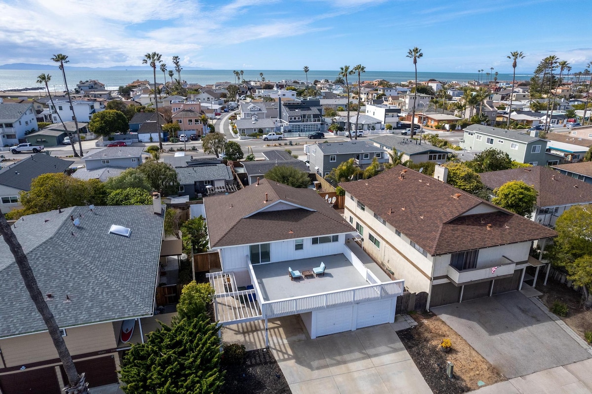 An aerial view showcases the townhouse location amidst a residential neighborhood, with palm trees dotting the landscape. The Pacific Ocean is visible in the distance, while a mix of angled roofs highlights the area’s coastal architecture.