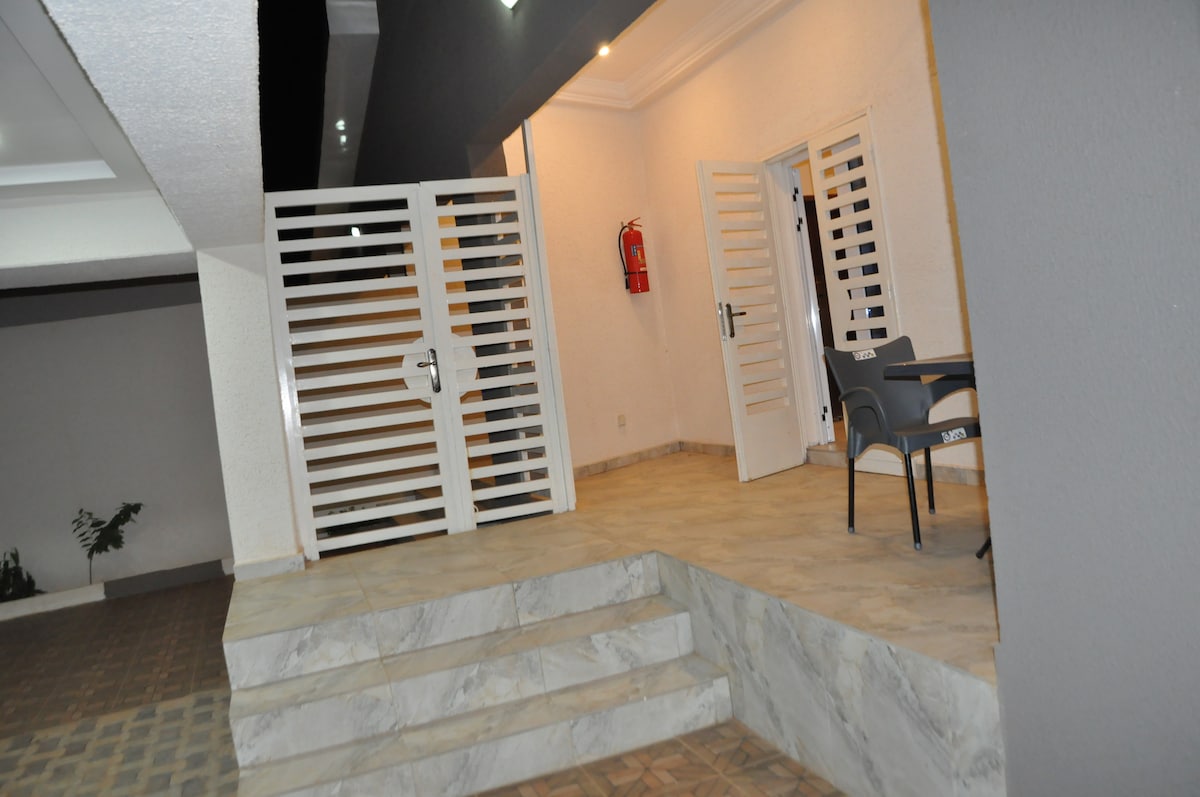 An entrance area features steps leading up to double doors, which are flanked by a fire extinguisher mounted on the wall. A single chair is visible on one side, while the space is illuminated by ceiling lights, enhancing the modern design.
