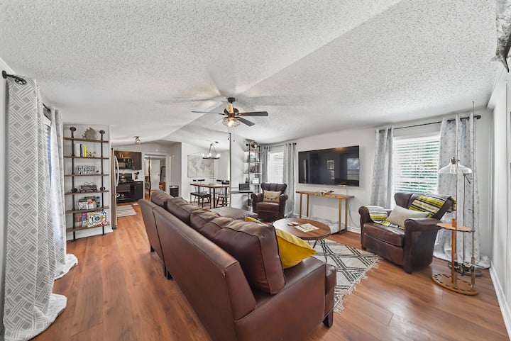 Open-concept living room with leather seating, 65” Smart TV, and natural light flowing in from multiple windows