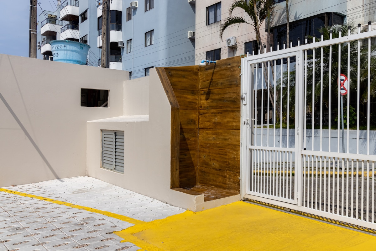 An entrance area is depicted with a modern gate and a wooden accent wall. The pavement features a yellow pathway leading into the property, while the surrounding buildings add a sense of urban environment. Natural light illuminates the space, enhancing visibility.