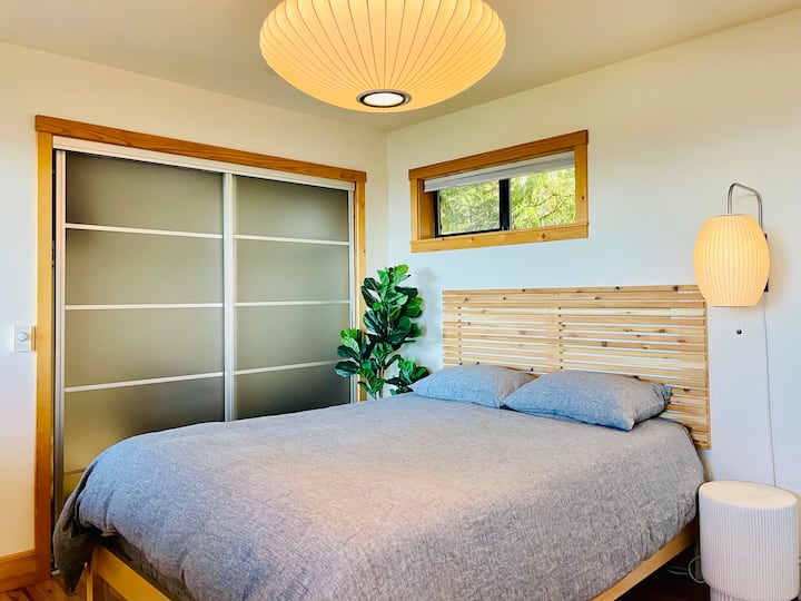 Dormitorio de nivel inferior con cama tamaño queen.  La habitación también cuenta con un área de trabajo con escritorio, monitor, teclado, ratón y cámara web.