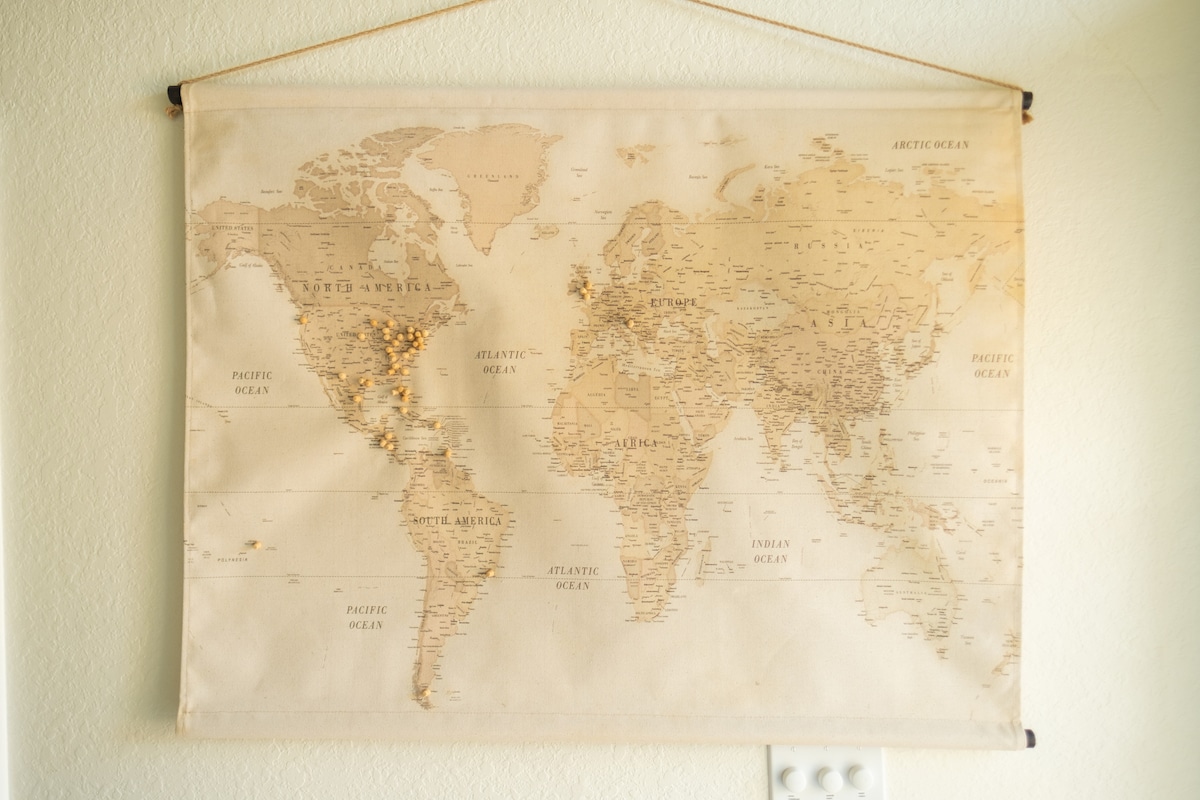 A world map is displayed on a hanging fabric canvas, featuring detailed geographical outlines and labeled countries. The map shows soft beige tones with subtle earth-toned accents, creating a visually calming effect in the space.