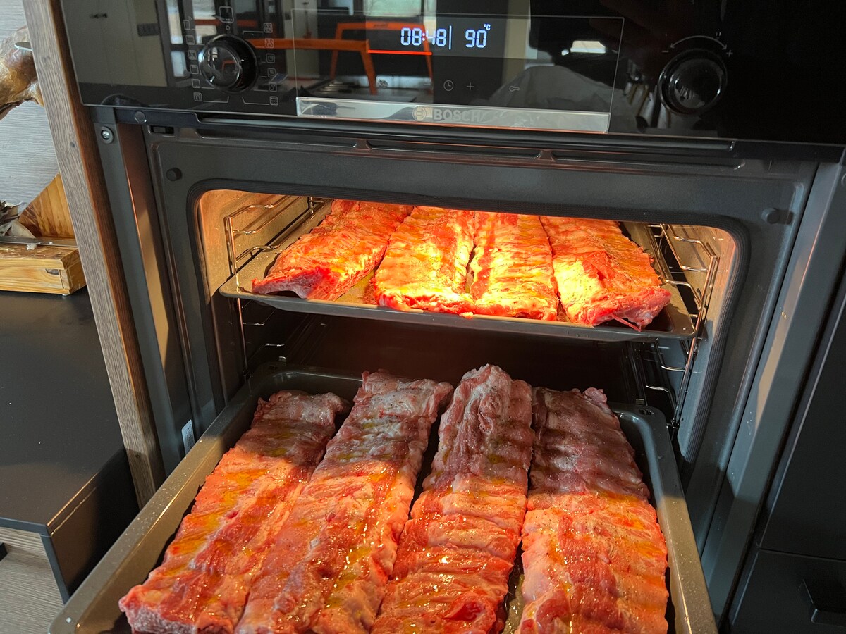 Two levels of an oven are displayed, each tray filled with raw ribs. The ribs are arranged neatly, showcasing a vibrant marbled texture. A display panel on the oven indicates a time setting of 08:41 and a temperature of 90 degrees.