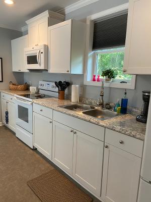 A well-equipped kitchen features white cabinetry and a granite countertop. Essential appliances include a microwave, stove, and coffee maker. Natural light enters through a window above the sink, which overlooks the surrounding greenery. A dish rack and utensils are neatly arranged for convenience.