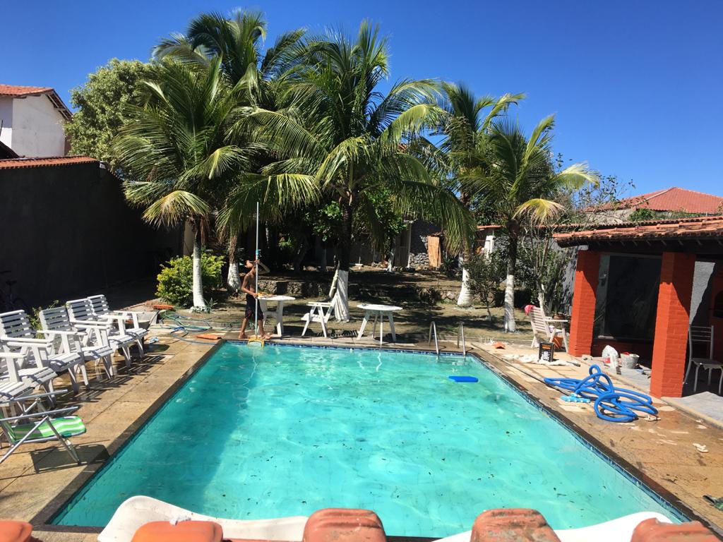 The private backyard features a pool surrounded by palm trees and lounge chairs. A covered barbecue area is present to the right, with a path leading through greenery. Sunlight illuminates the inviting water, creating a refreshing atmosphere.