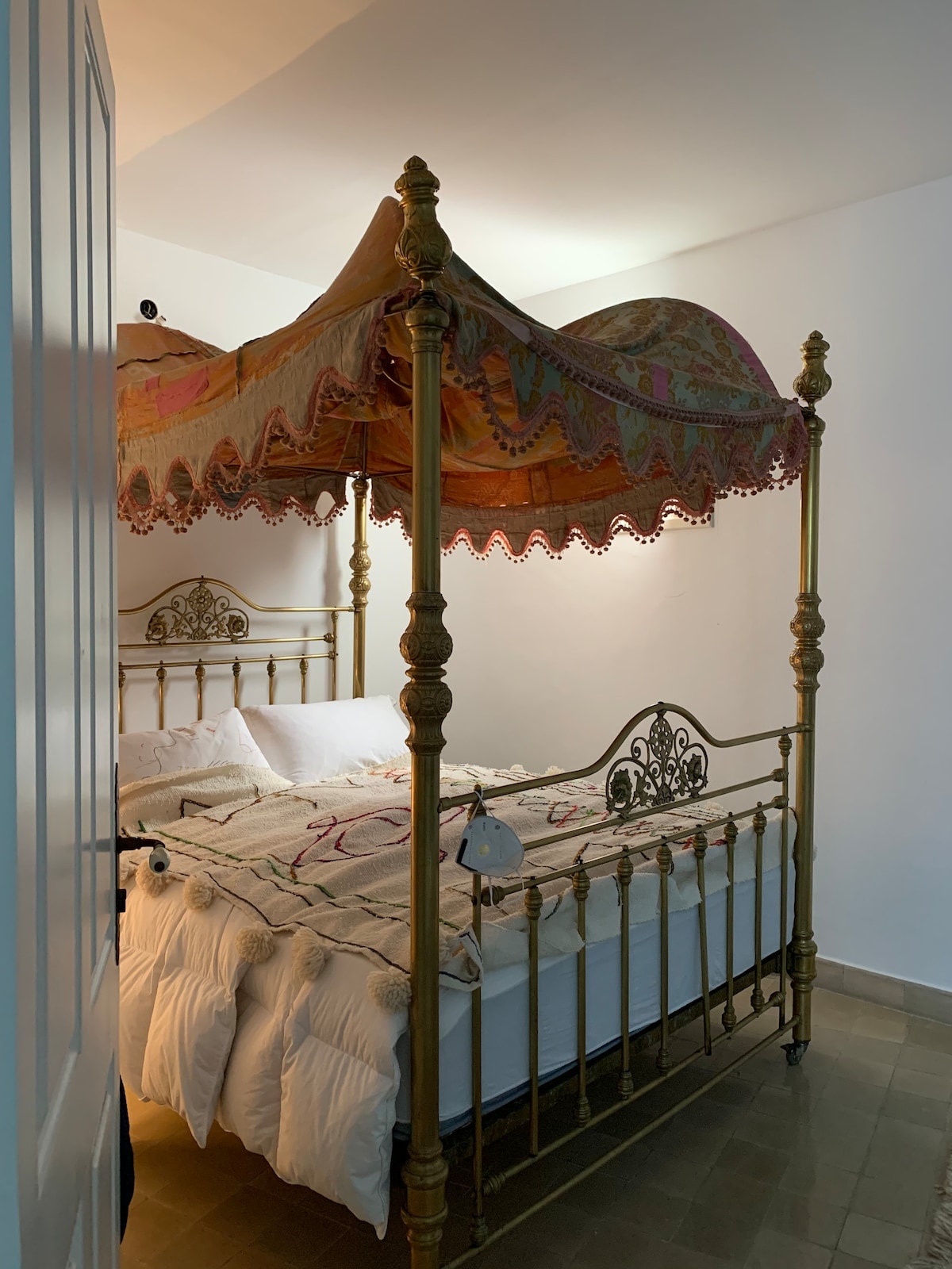 A spacious bed is featured under an ornate, draped canopy that adds a touch of elegance. Soft lighting creates a serene environment, while intricate designs on the canopy enhance the overall aesthetic of the room.