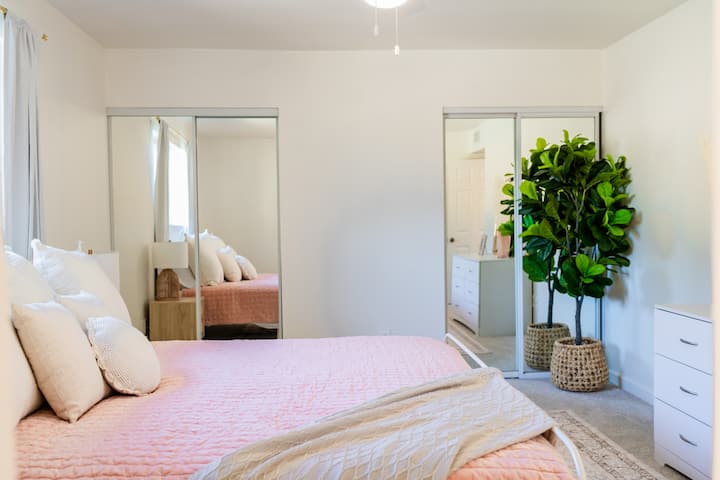 Pumzika kwenye kitanda cha kifalme chenye starehe ukiwa na blanketi laini la rangi ya waridi na mito ya kitani, vyote vikiwa vimewekwa kwenye mandharinyuma tulivu, yenye rangi nyeupe angavu.