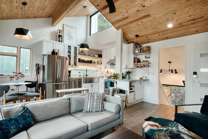 Изглед към напълно заредена кухня от всекидневната. Стълбища, водещи надолу към спалните вдясно.