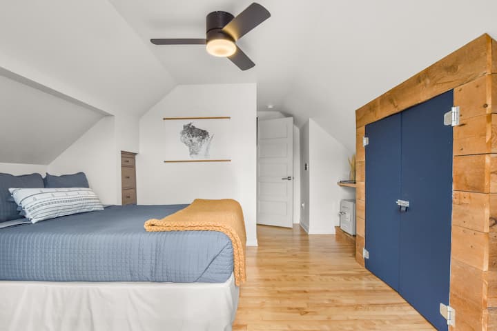 The first bedroom has a queen bed with cozy blankets, gets a lot of natural light, and is themed with reclaimed barn wood, navy and charcoal grey accents, and bits of Wisconsin!