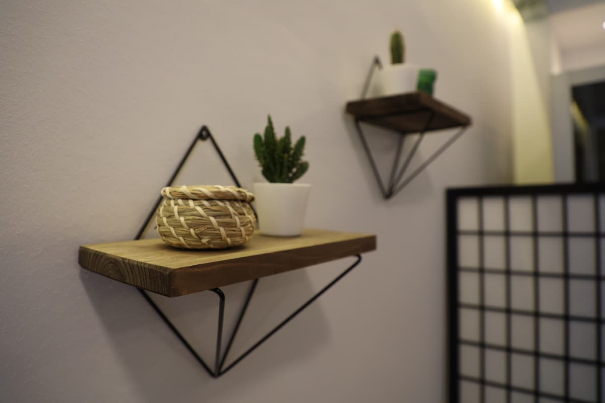 Wooden shelves with metal brackets are mounted on a light wall. A small woven basket and a white potted plant are displayed on one shelf, while a green succulent is positioned on the other, adding a touch of nature to the interior.