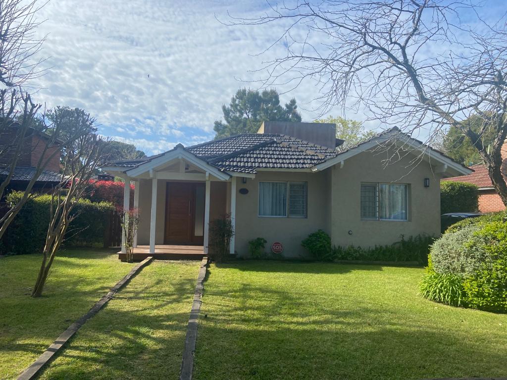 A single-story house is presented with a welcoming entrance, featuring a sloped roof and front porch. The well-maintained lawn is bordered by trees and shrubs, creating a peaceful outdoor space. Natural light brightens the exterior, complemented by a clear sky above.