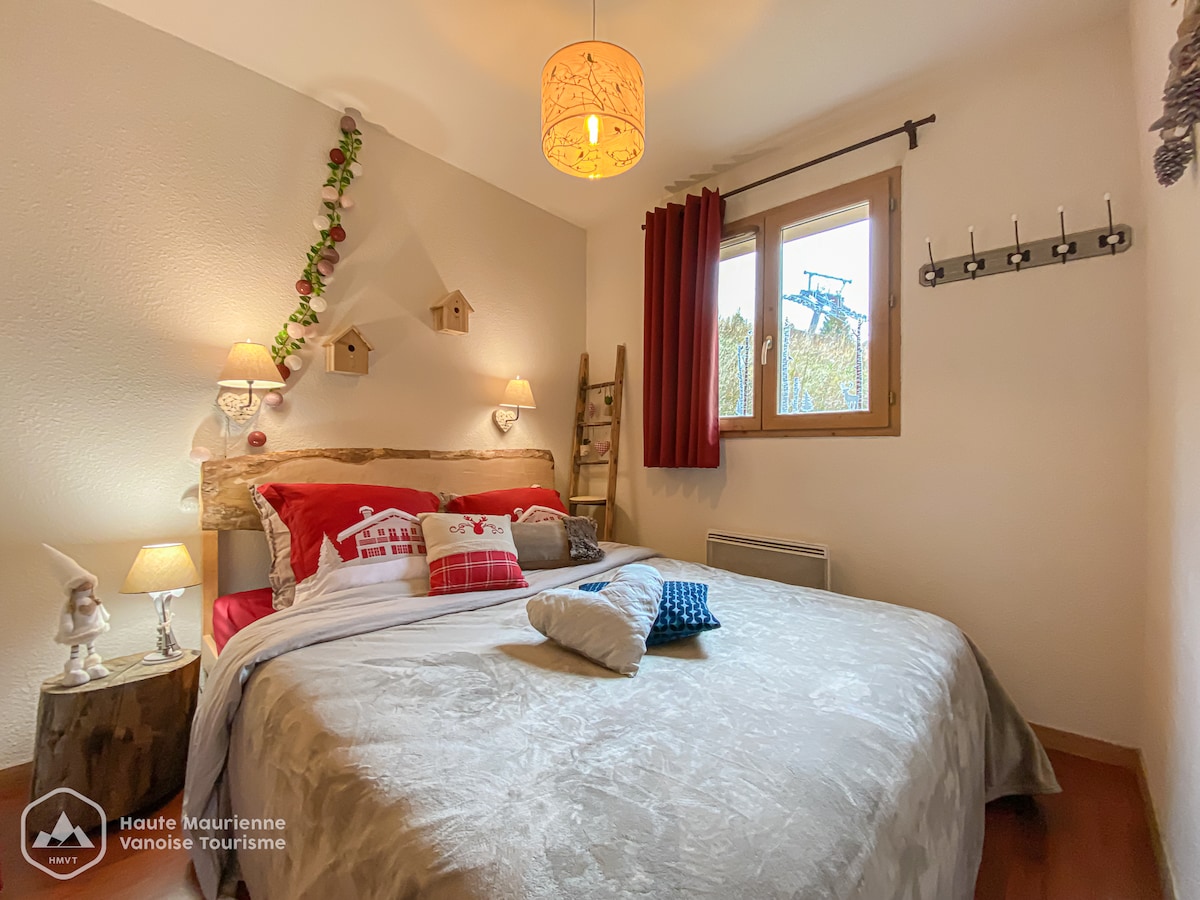 A cozy bedroom features a spacious bed adorned with soft bedding and decorative pillows. Two bedside lamps provide gentle illumination. A window allows natural light to fill the room, while holiday-themed decorations and wooden accents enhance the inviting setting.