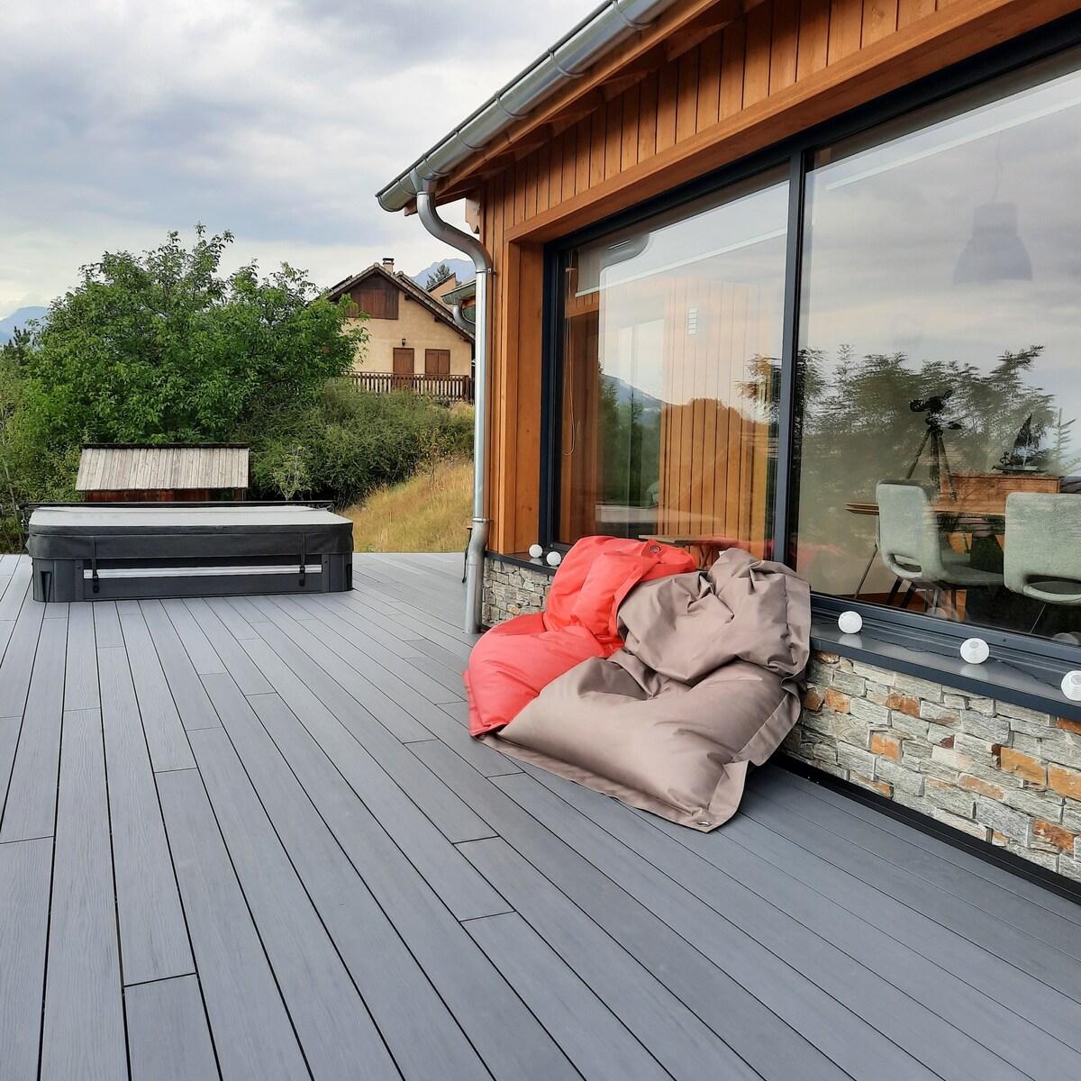 An inviting outdoor terrace features a well-maintained hot tub and cozy bean bags in vibrant colors. The wooden structure with large windows allows for beautiful views of the surrounding nature. The decking appears spacious, enhancing the area for relaxation and enjoyment.