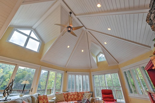 A spacious living area is highlighted by a soaring, angled ceiling adorned with recessed lighting. Large windows allow ample natural light and showcase scenic views of the surrounding landscape. Comfortable seating is arranged around a cozy fireplace, enhancing the room's openness and inviting atmosphere.