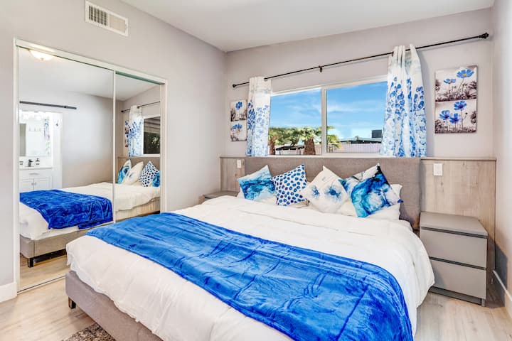 Serene Master Retreat: cama King con TV y baño adjunto con ducha completa e inodoro. Disfruta de las vistas del oasis del patio con palmeras, plantas, césped artificial, columpio y chimenea. Navy Blue Tonal Bliss in a Tranquil Haven