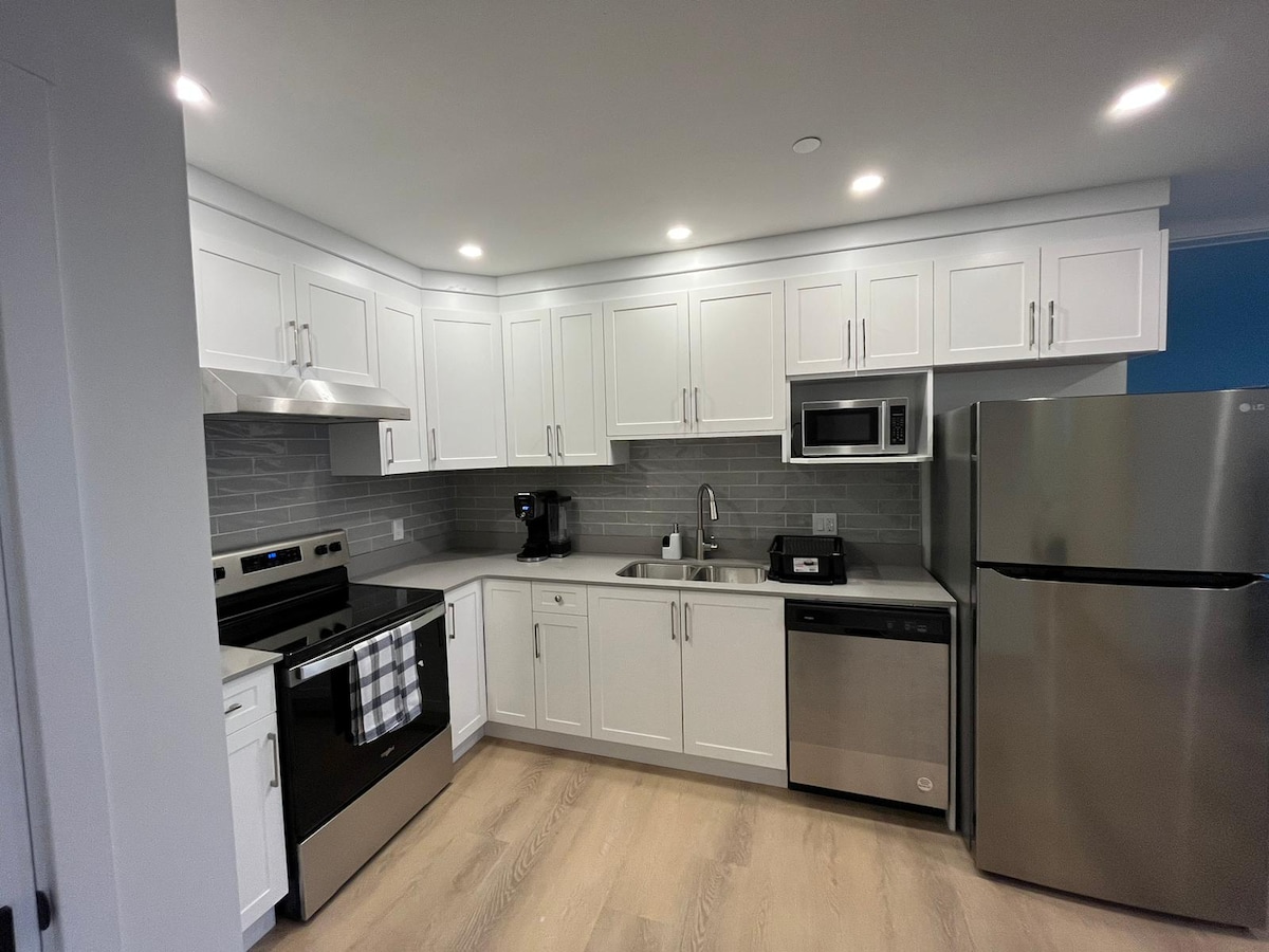 A well-equipped kitchen features modern stainless steel appliances, including a refrigerator, stove, and microwave. White cabinetry contrasts with gray backsplash tiles, while a coffee maker and sink are positioned for convenience. Ample counter space is available for meal preparation, enhancing functionality.