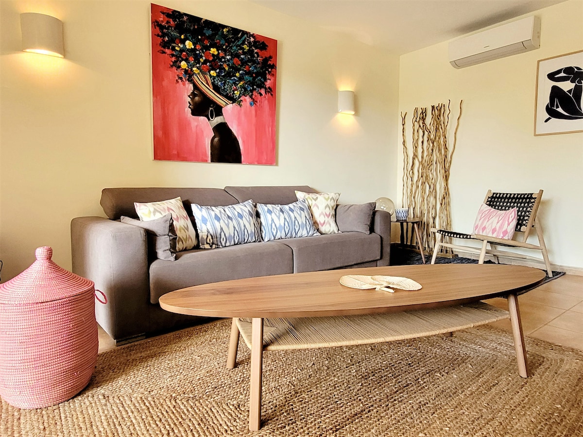 A spacious living area features a comfortable sofa adorned with decorative pillows, next to a wooden coffee table with a natural finish. An eye-catching artwork hangs on the wall, while soft lighting creates a cozy ambiance. A textured area rug adds warmth to the space.