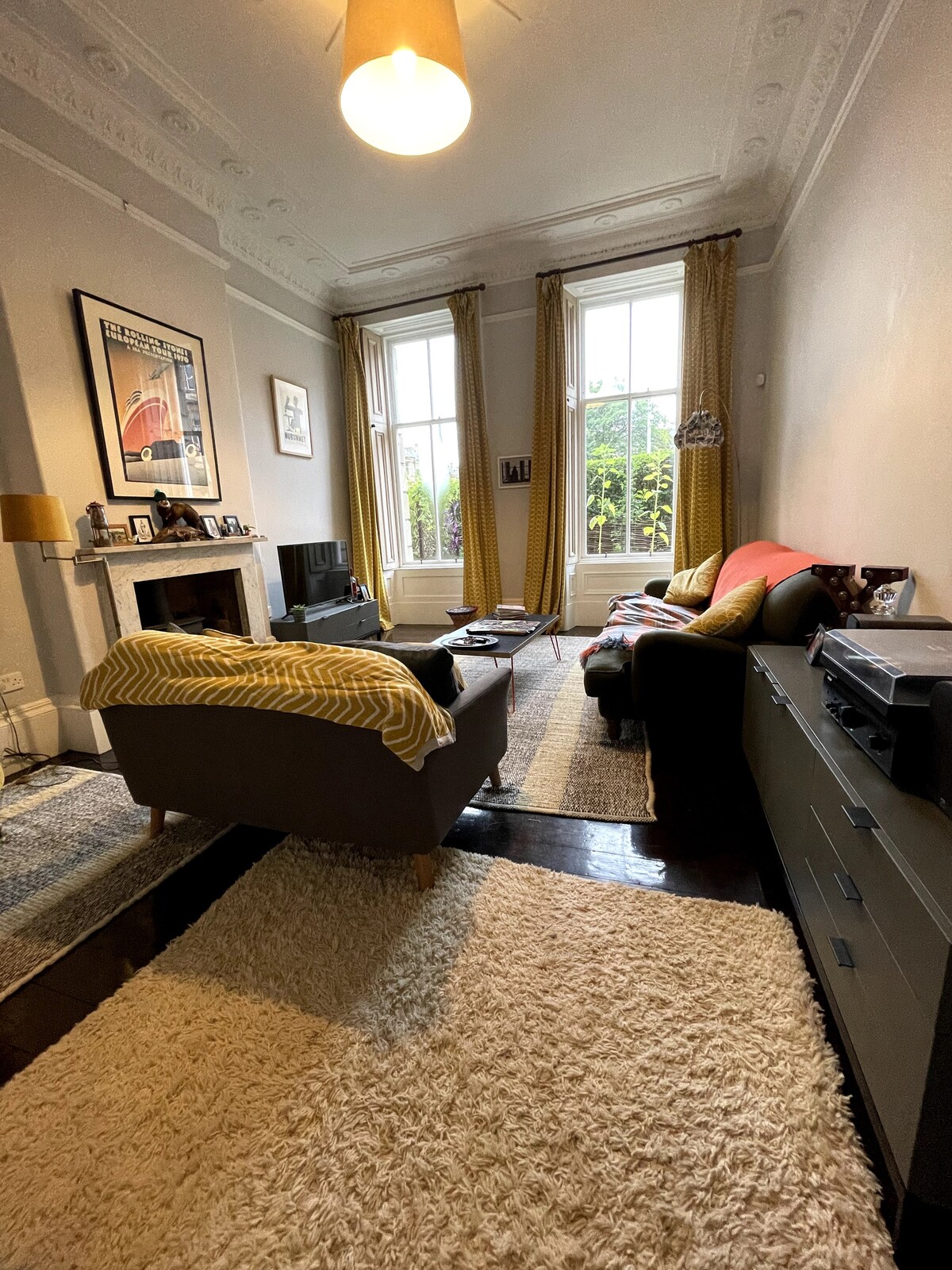 A spacious sitting room is highlighted by large windows that allow natural light to illuminate the area. Comfortable seating arrangements include a sofa and armchairs. A soft area rug covers the floor, while decorative art pieces adorn the walls, adding character to the room.