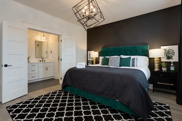 Recámara con cama tamaño king, cabecera acolchada de color verde esmeralda, ropa de cama color carbón y lámparas colgantes