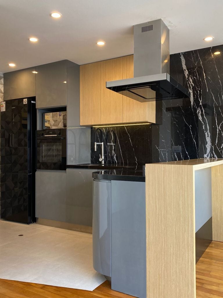 The kitchen features modern cabinetry in contrasting shades of grey and light wood. A sleek black marble backsplash adds sophistication, while under-cabinet lighting enhances the space. Stainless steel appliances, including a built-in oven and refrigerator, complement the contemporary design.