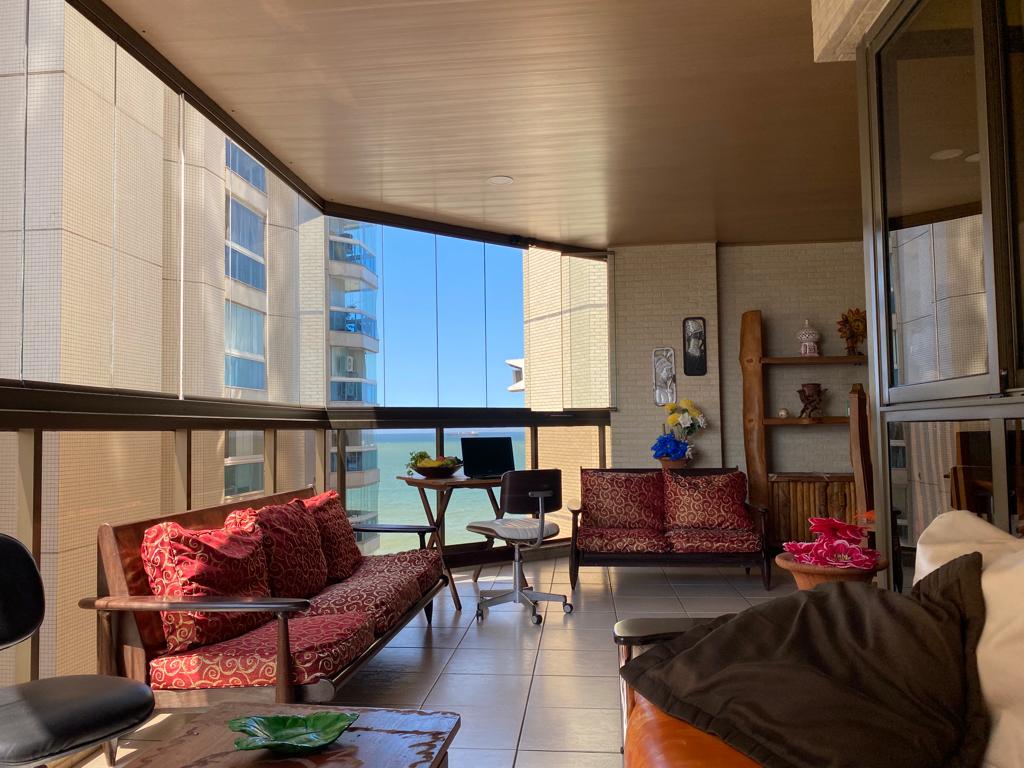 An inviting balcony space features comfortable seating arrangements with decorative cushions. A small table with a chair is positioned for potential workspace. Large windows allow for a panoramic view of the ocean, enhancing the airy ambiance of the area.