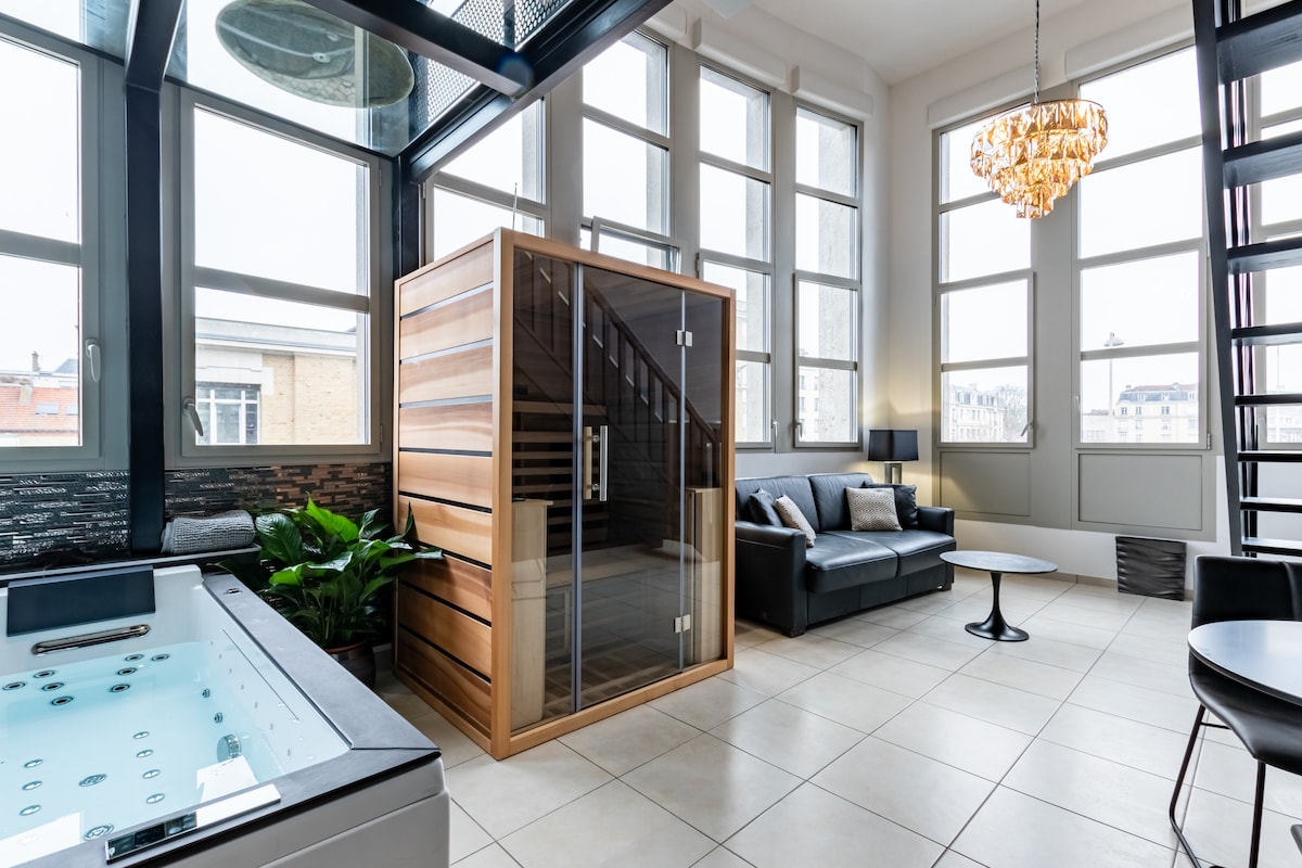An inviting spa area showcases a wooden sauna with glass doors, complemented by a spacious leather sofa and modern coffee table. Natural light floods in through large windows, highlighting the elegant tile flooring and greenery positioned nearby.