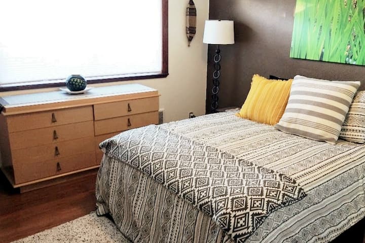 The main bedroom features a vintage MCM light wood long dresser, comfy bed and an original photo of the tall grass from Point St. George beach and lookout.