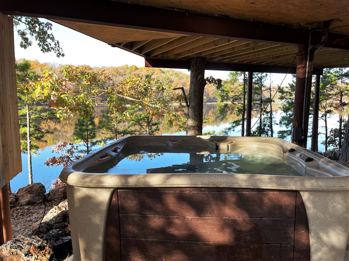 A private hot tub is situated on a spacious deck, offering serene views of Sayersbrook Lake. The calm water reflects the trees and autumn foliage surrounding the area, creating a peaceful atmosphere for relaxation.