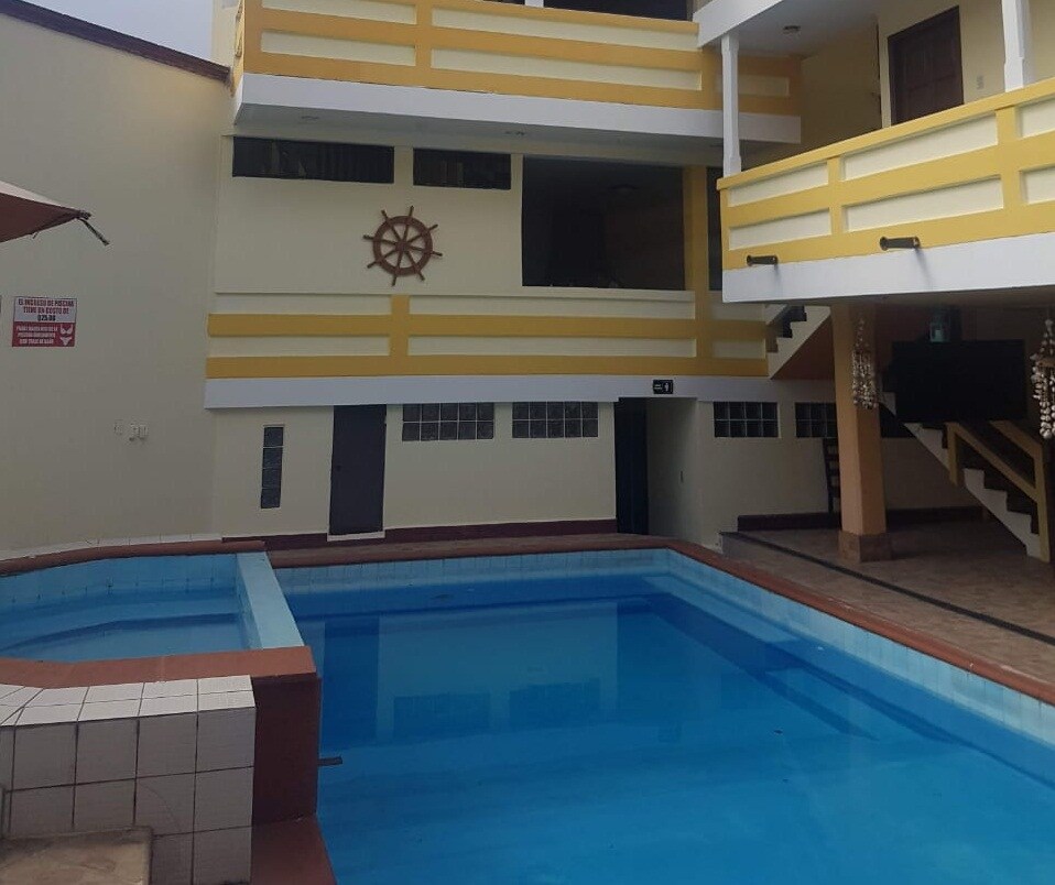 A rectangular swimming pool is positioned at the center of the courtyard, surrounded by two levels of connected balconies with yellow railings. Staircases lead to upper floors, and a nautical-themed decorative element is visible on the wall.