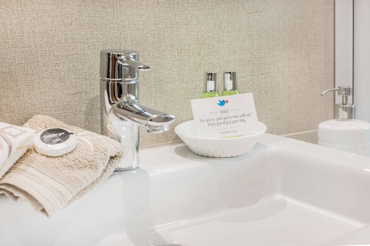 The bathroom sink area features modern fixtures with a sleek faucet, complemented by neatly arranged toiletries in a small dish. Soft towels are placed beside the sink, while a decorative soap dispenser adds a clean touch to the setup.