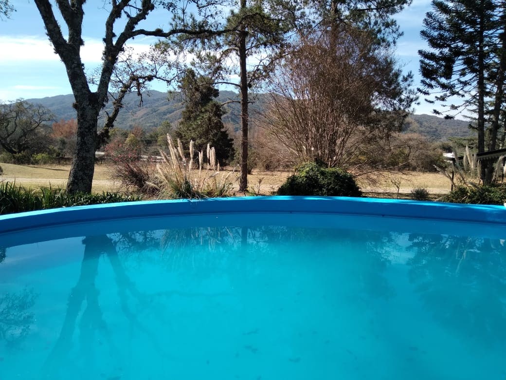 A shimmering swimming pool is set against a backdrop of lush greenery and rolling hills. The clear blue water reflects the surrounding trees, inviting relaxation and connection with nature.