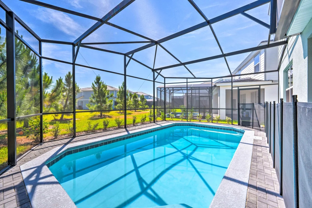 A private pool is enclosed by a screened lanai, providing a safe and comfortable swimming area. Sunlight reflects off the clear water, while a spacious deck surrounds the pool. Lush greenery is visible beyond the enclosure, offering a serene outdoor view.