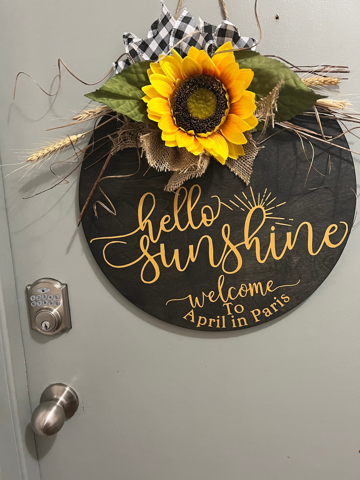 A circular welcome sign is displayed on the door, featuring the words 'hello sunshine' in elegant script. A sunflower and decorative elements, including wheat and a checkered bow, add a cheerful touch.
