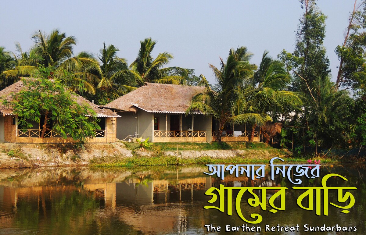 The image features rustic mud houses with thatched roofs, situated beside a calm water body. Lush green palm trees and vegetation complement the serene landscape, creating a tranquil atmosphere that reflects the natural beauty of the Bengali countryside.