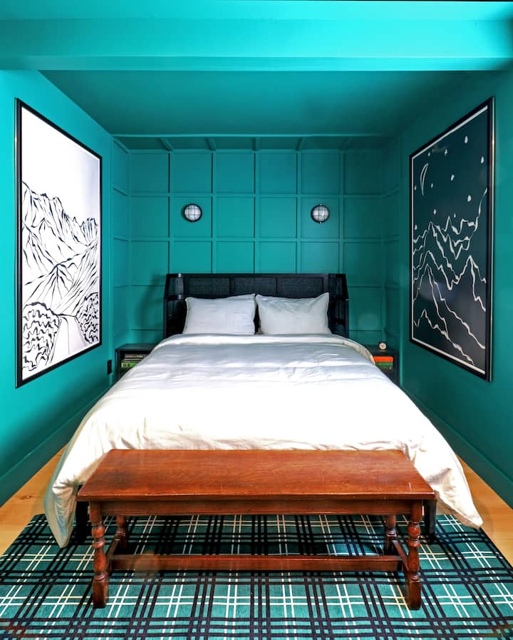 Green room with a queen bed, with oversized artwork and black and white accents