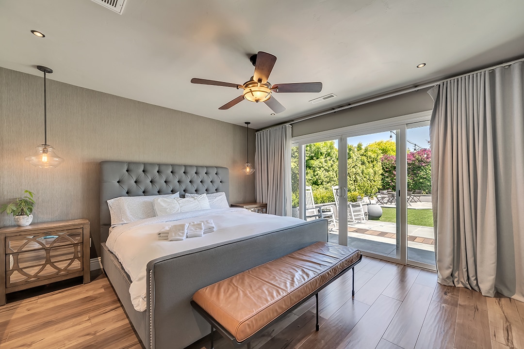 Master slaapkamer met kingsize bed, hanglampen, verzonken lampen, plafondventilator, verduisteringsgordijnen en glazen schuifdeuren die naar de achtertuin leiden