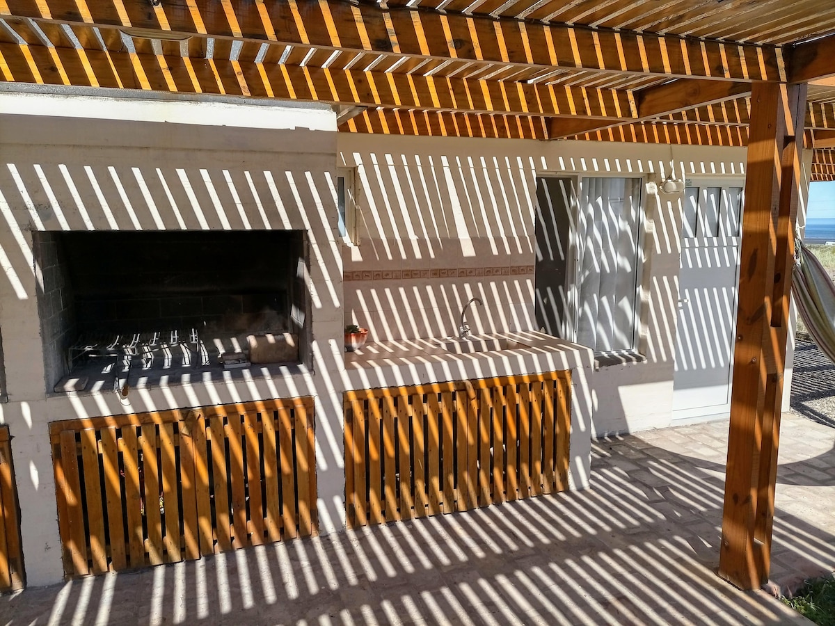 A shaded outdoor area features a grill and a preparation space, with wooden elements creating a pattern of light and shadow. A hammock can be seen in the corner, suggesting a comfortable spot for relaxation.