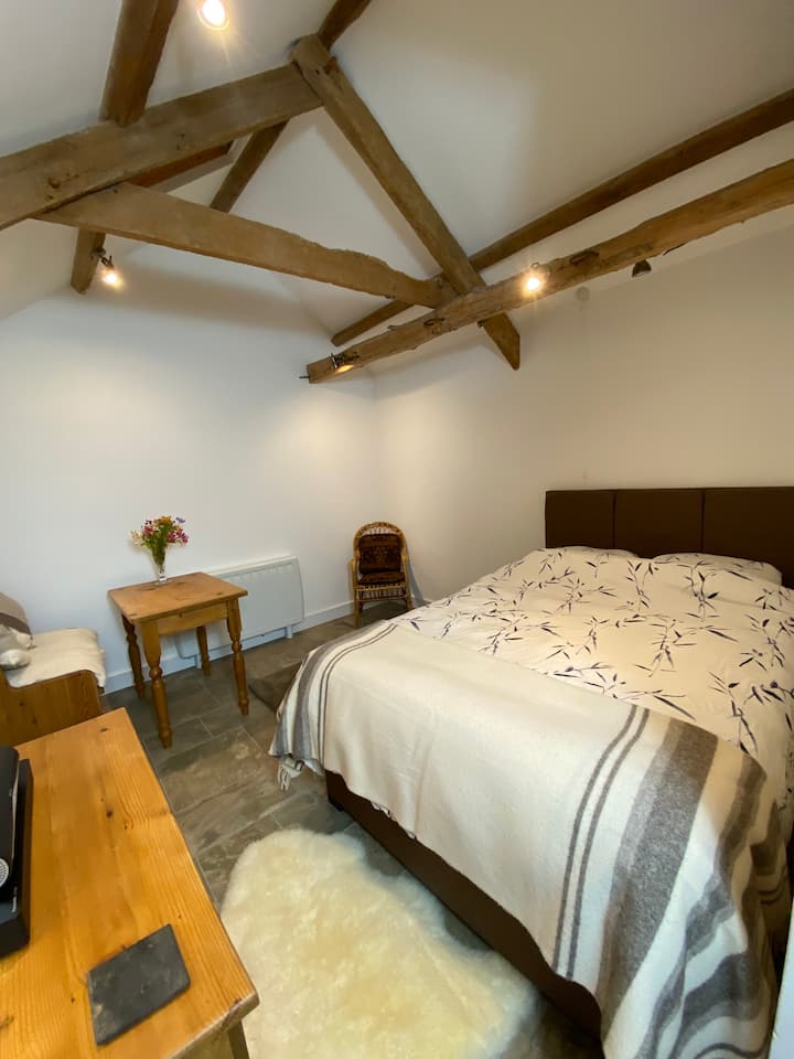 غرفة نوم اسطبلات بسرير مزدوج ومنطقة صغيرة لتناول الطعام (على اليسار) بالإضافة إلى تلفزيون ذكي. 