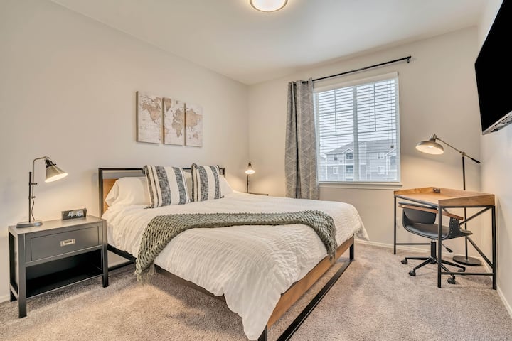 חדר שינה ראשי עם טלוויזיה 4K ושולחן עבודה עם שקעי חשמל ו - USB משולבים.